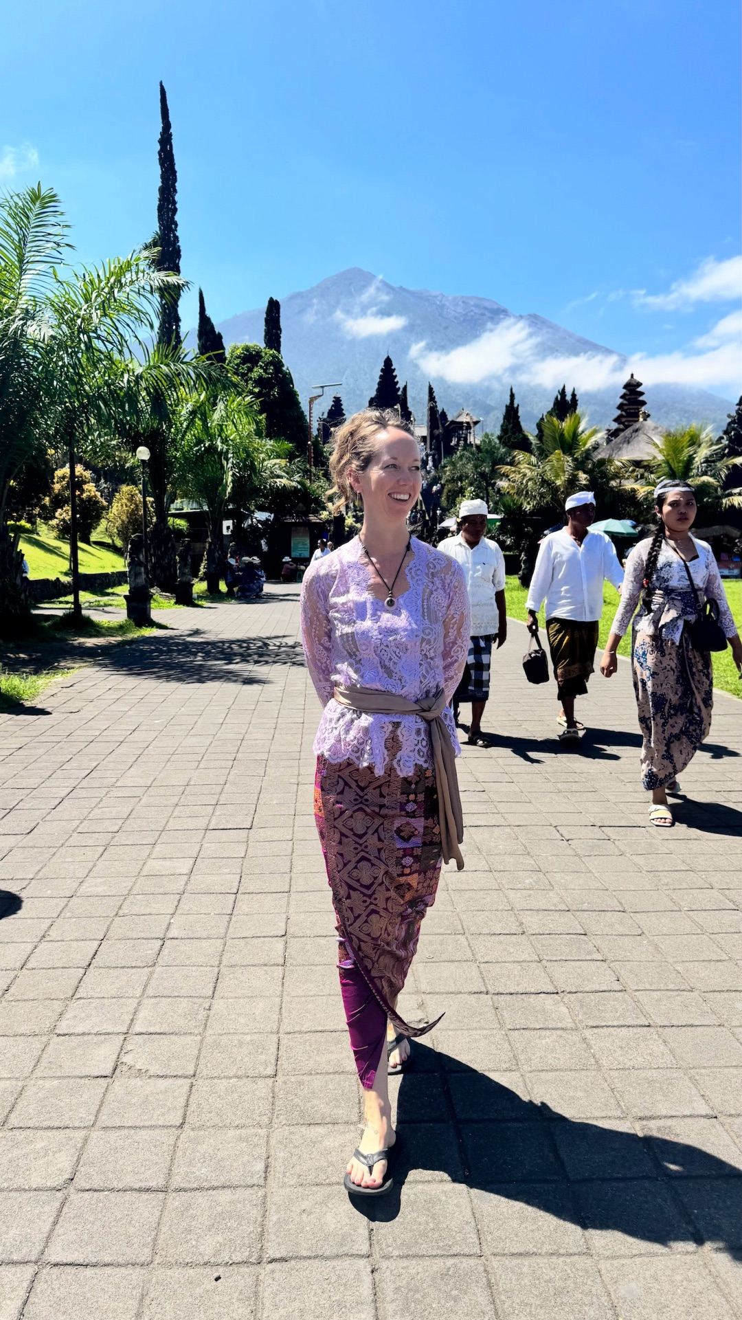 Mira Mi walking in traditional Balinese ceremonial dress at Besakih Mother Temple, Mount Agung behind her
